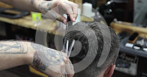 Close up of Â hairdresser`s hands cutting short hair of middle aged man using a hairbrush and scissors.